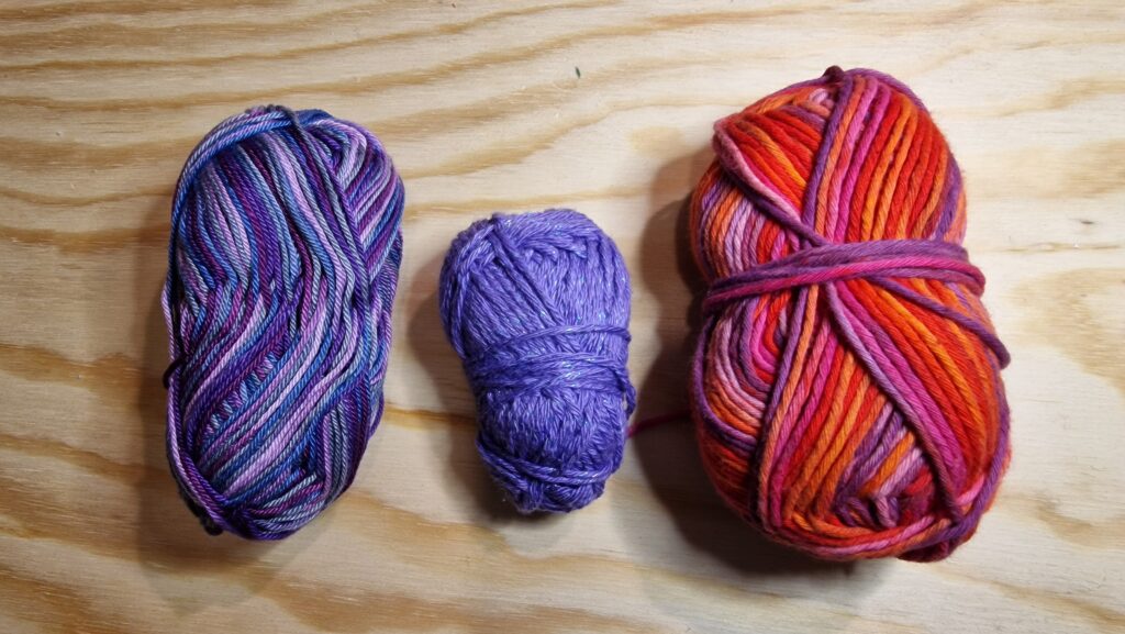 "Trois pelotes pour le collier 5 : rouges, violets et un fil argenté lumineux."