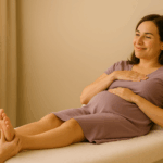 Femme enceinte souriante allongée sur une table de massage, recevant une séance de réflexologie plantaire dans un cadre lumineux et apaisant à Morges.